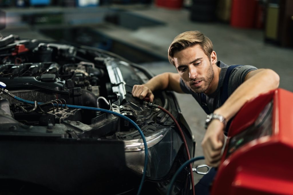 Young mechanic maintaining AC unit of a car at auto repair shop.